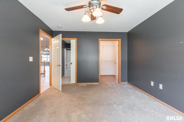 unfurnished bedroom with a walk in closet, baseboards, carpet, a closet, and ceiling fan