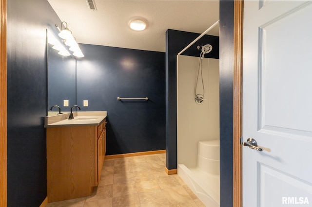 bathroom with a shower, vanity, tile patterned floors, and baseboards