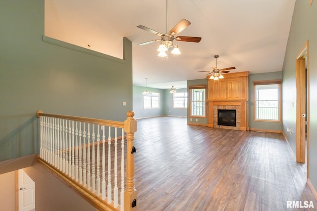 unfurnished living room featuring wood finished floors, ceiling fan, baseboards, lofted ceiling, and a tile fireplace