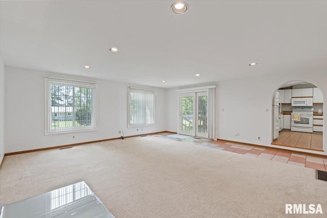 unfurnished living room with light colored carpet, recessed lighting, baseboards, and arched walkways