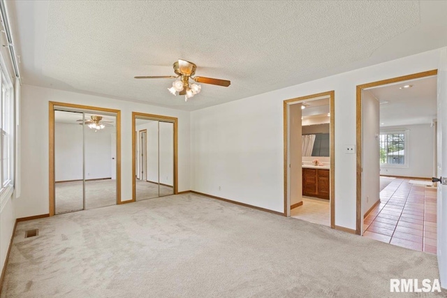 unfurnished bedroom featuring two closets, carpet, baseboards, a textured ceiling, and connected bathroom