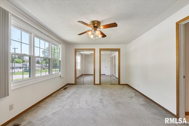 unfurnished bedroom with multiple closets, light carpet, baseboards, a textured ceiling, and a ceiling fan