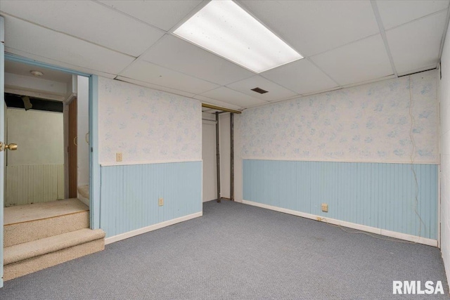 finished below grade area featuring a wainscoted wall, wallpapered walls, carpet, a paneled ceiling, and stairs