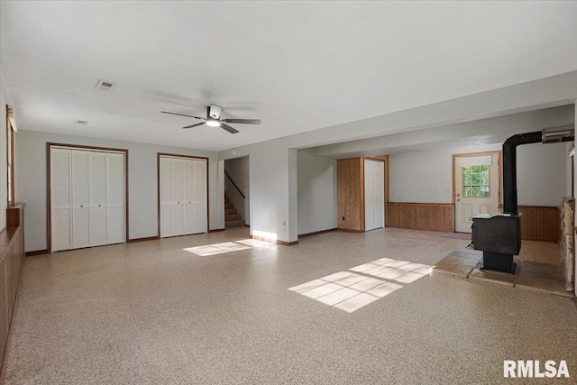 1401 265th St, Sherrard, IL 61281 - unfurnished living room with wainscoting, stairway, ceiling fan, a wood stove, and baseboards