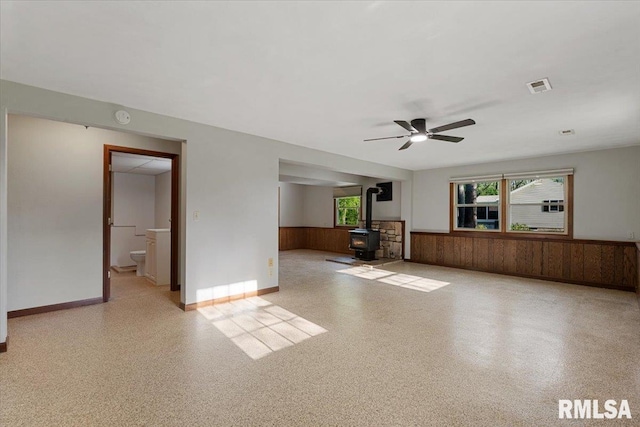 1401 265th St, Sherrard, IL 61281 - unfurnished living room with wainscoting, a wood stove, a ceiling fan, and wood walls