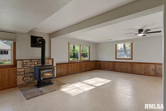 1401 265th St, Sherrard, IL 61281 - unfurnished living room with wainscoting, healthy amount of natural light, wooden walls, a wood stove, and a ceiling fan