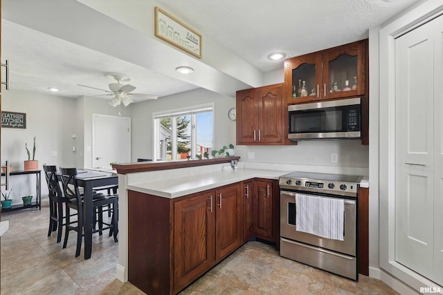 13218 300th St, Donahue, IA 52746 - kitchen featuring appliances with stainless steel finishes, a peninsula, light countertops, a ceiling fan, and glass insert cabinets