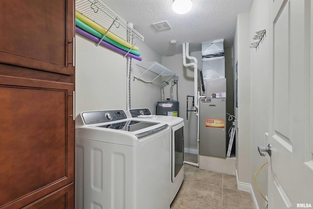 clothes washing area with separate washer and dryer, water heater, a textured ceiling, light tile patterned flooring, and baseboards
