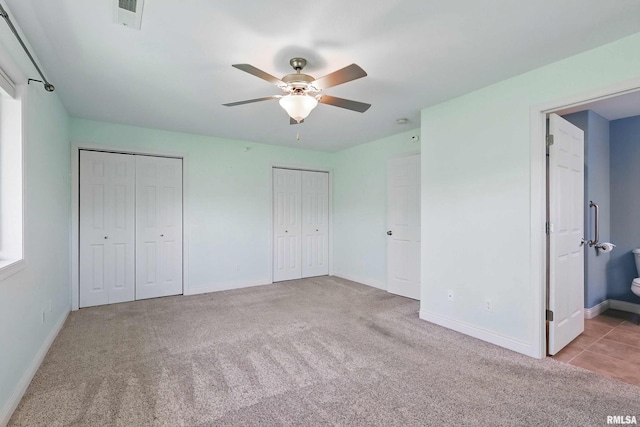 unfurnished bedroom featuring two closets, carpet flooring, baseboards, and ensuite bathroom