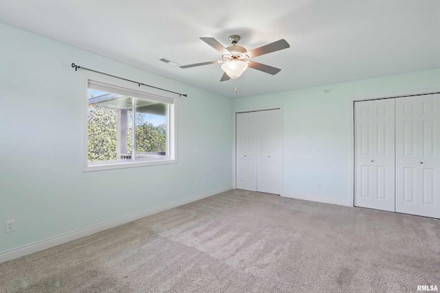 unfurnished bedroom featuring multiple closets, baseboards, light colored carpet, and ceiling fan