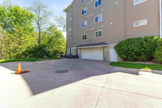 view of property exterior with an attached garage, concrete driveway, a fire pit, and central air condition unit