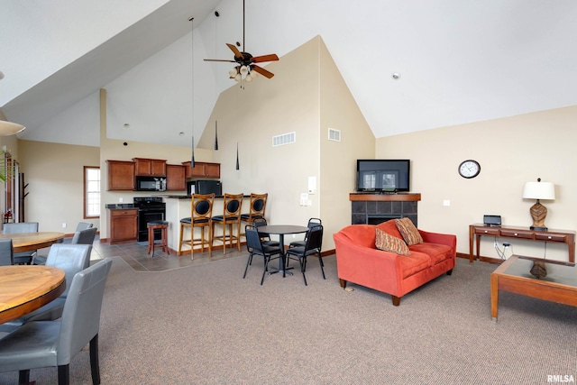 carpeted living room with high vaulted ceiling, ceiling fan, a tiled fireplace, and baseboards