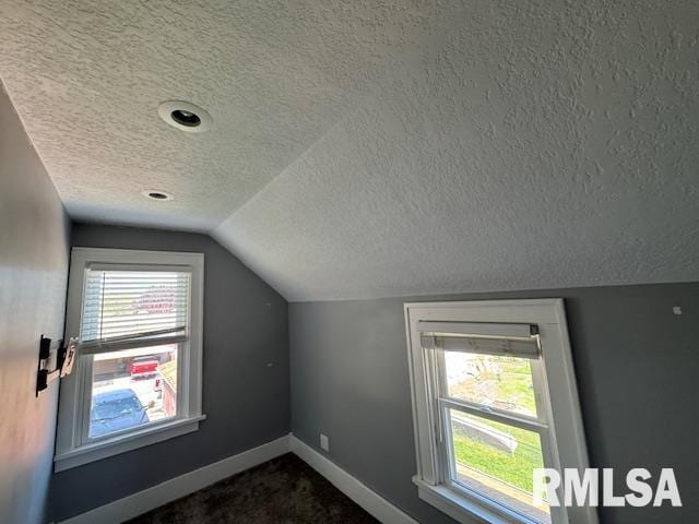 bonus room with a textured ceiling, lofted ceiling, baseboards, and dark colored carpet