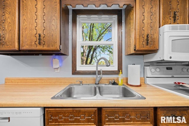 kitchen featuring a sink, white appliances, light countertops, and brown cabinetry