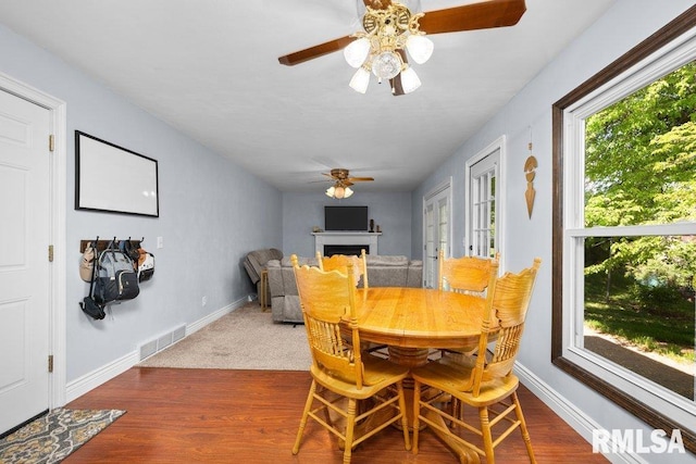 dining area featuring ceiling fan, a fireplace, wood finished floors, and baseboards