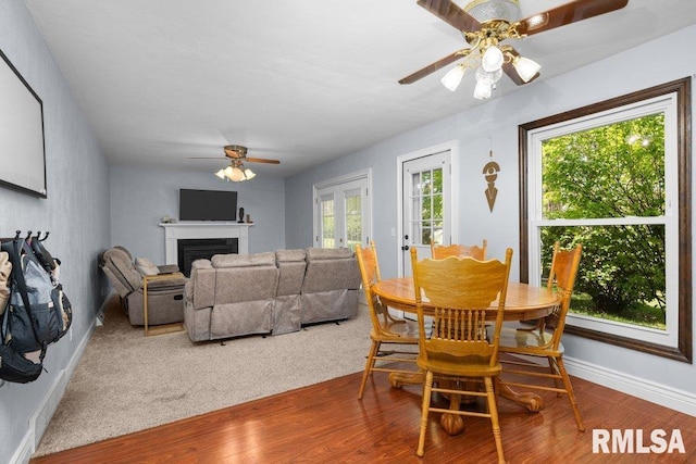 dining space featuring a ceiling fan, wood finished floors, baseboards, and a fireplace