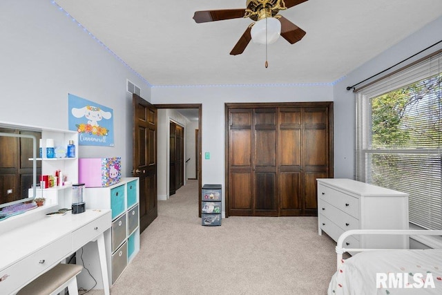 bedroom with light colored carpet, a desk, a ceiling fan, and a closet
