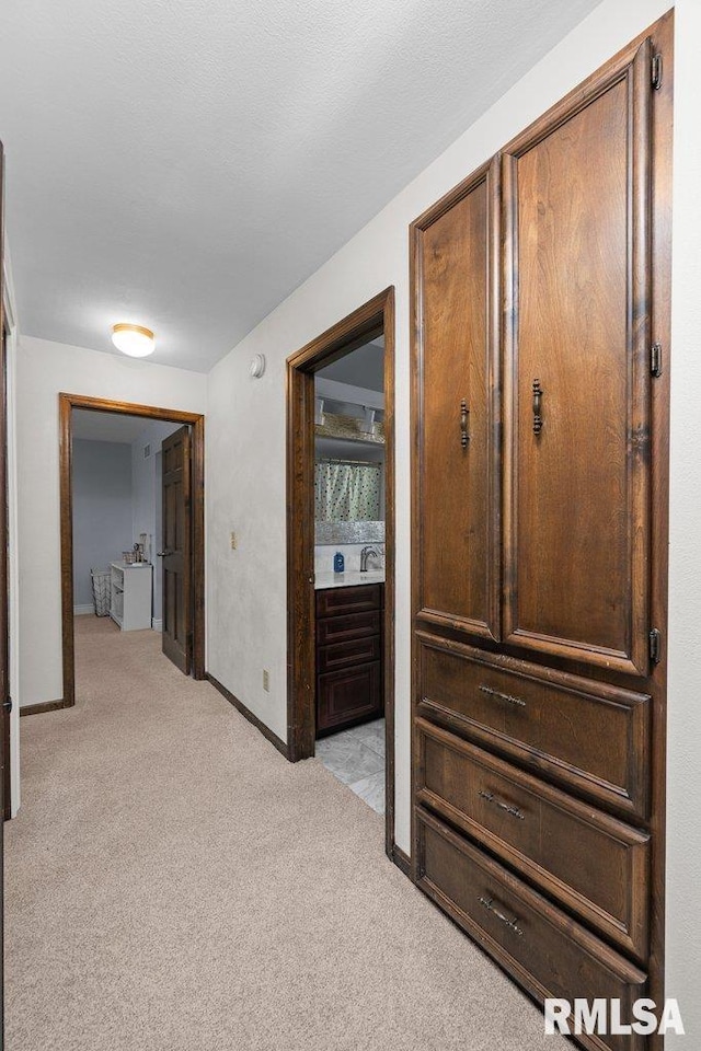 hallway with light colored carpet, baseboards, and a sink