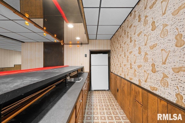 kitchen with freestanding refrigerator, a paneled ceiling, wallpapered walls, a wainscoted wall, and a sink