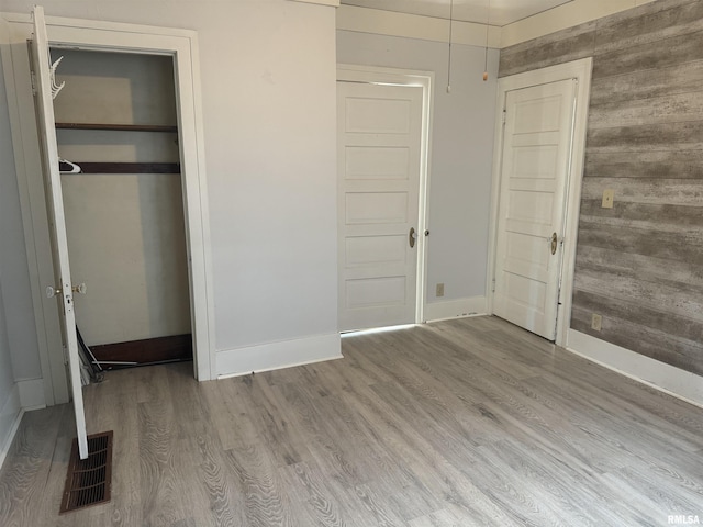unfurnished bedroom with baseboards, wood finished floors, a closet, and wood walls