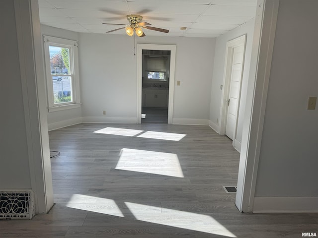 unfurnished bedroom with a drop ceiling, baseboards, wood finished floors, and ceiling fan