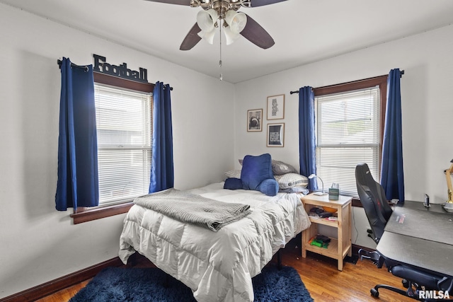 bedroom featuring wood finished floors, multiple windows, a ceiling fan, and baseboards