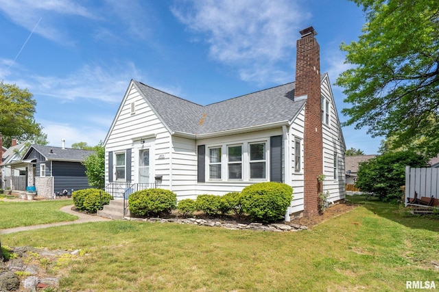 view of front facade with a shingled roof, a chimney, and a front lawn