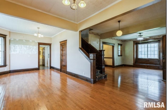 unfurnished living room featuring a chandelier, wood finished floors, baseboards, crown molding, and stairs