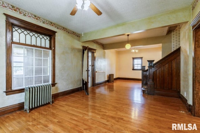 unfurnished living room with radiator, light wood-style floors, baseboards, stairs, and ceiling fan