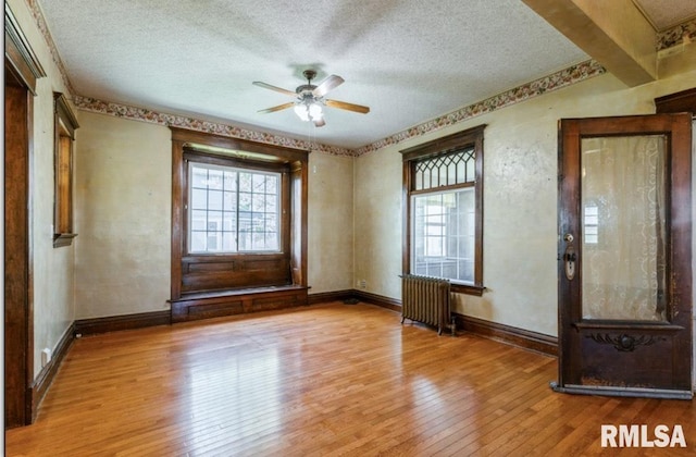 spare room with radiator heating unit, a textured ceiling, hardwood / wood-style flooring, ceiling fan, and baseboards