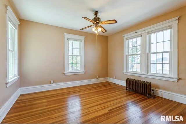 spare room with radiator, wood finished floors, ceiling fan, and baseboards