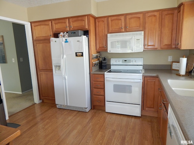 kitchen with white appliances, light wood finished floors, brown cabinetry, a sink, and light countertops