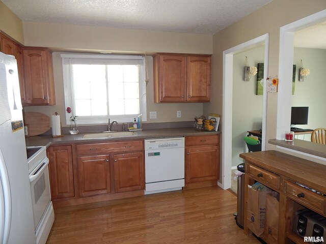 kitchen featuring white appliances, a sink, brown cabinets, light wood-type flooring, and dark countertops