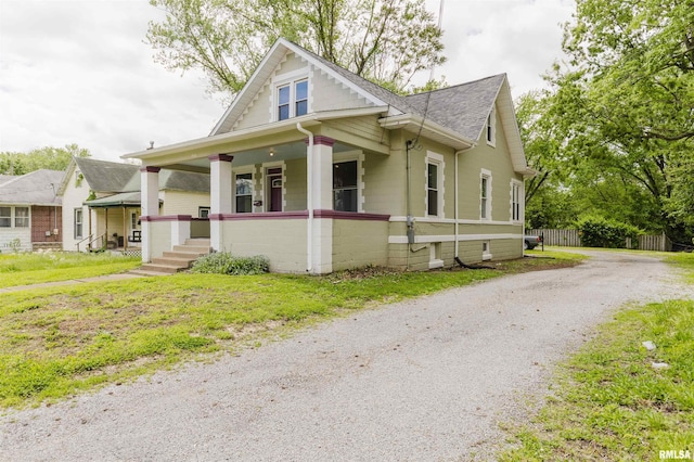 bungalow-style house featuring covered porch, roof with shingles, fence, and gravel driveway