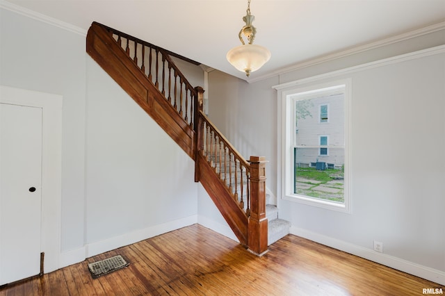stairway featuring baseboards, hardwood / wood-style floors, ornamental molding, and healthy amount of natural light