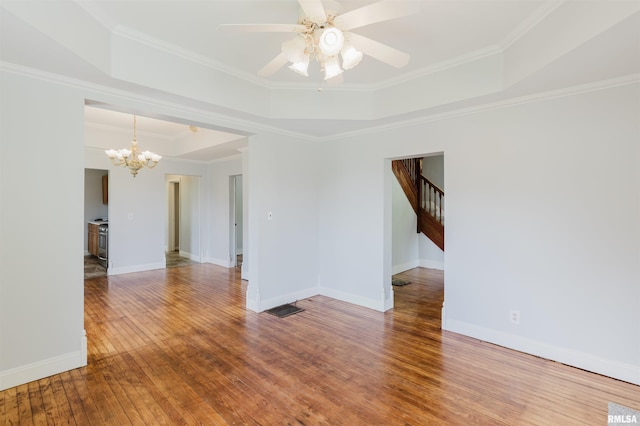 empty room with a raised ceiling, hardwood / wood-style flooring, a chandelier, ceiling fan, and ornamental molding