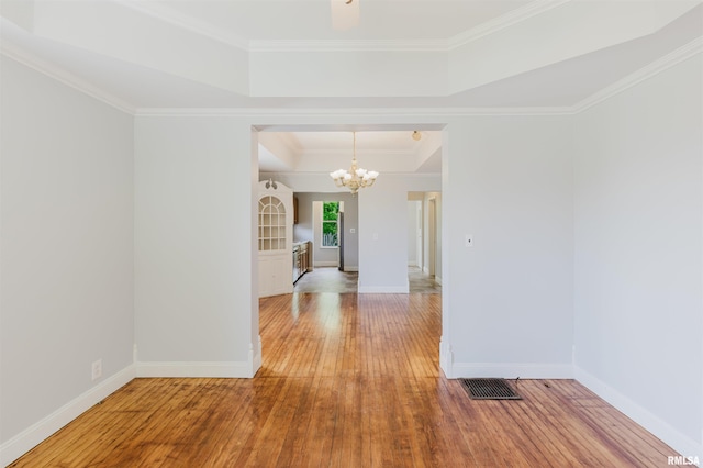 spare room featuring a chandelier, hardwood / wood-style flooring, crown molding, baseboards, and a tray ceiling