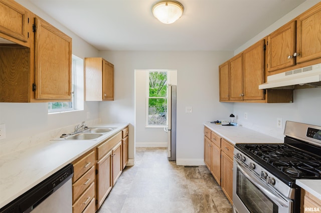 kitchen with appliances with stainless steel finishes, under cabinet range hood, a sink, and light countertops