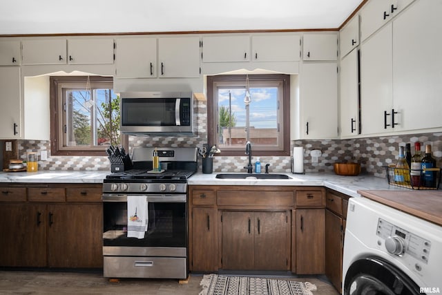 kitchen with washer / dryer, stainless steel appliances, a sink, light countertops, and decorative backsplash
