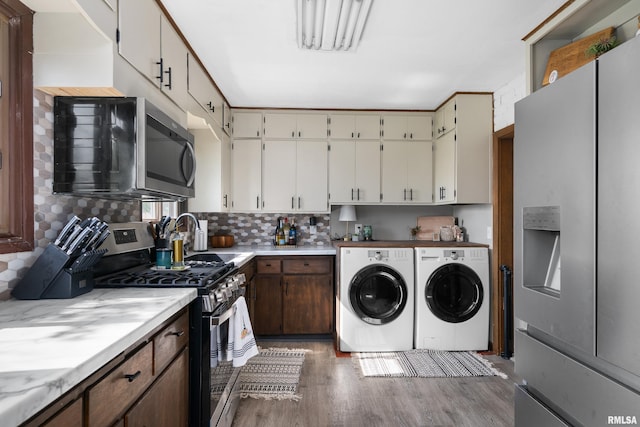 kitchen featuring stainless steel appliances, washing machine and dryer, wood finished floors, a sink, and decorative backsplash