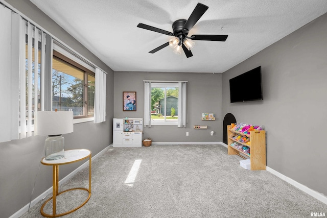 playroom featuring plenty of natural light, carpet flooring, ceiling fan, baseboards, and a textured ceiling
