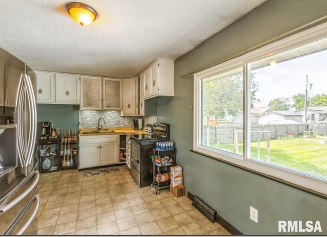 kitchen featuring appliances with stainless steel finishes, a sink, tasteful backsplash, white cabinetry, and a textured ceiling