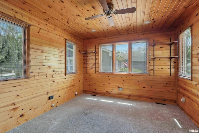 carpeted spare room featuring healthy amount of natural light, wooden walls, ceiling fan, and wooden ceiling
