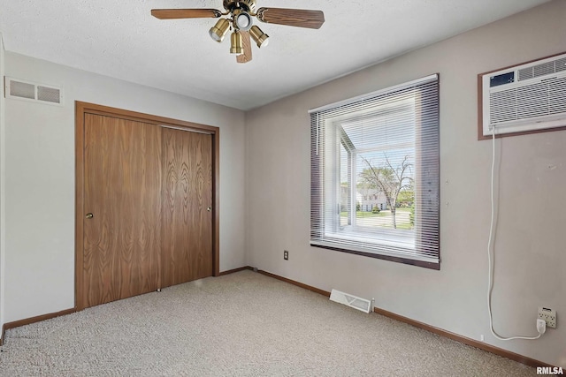 unfurnished bedroom with light colored carpet, a wall unit AC, baseboards, a closet, and a ceiling fan