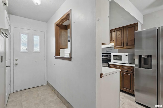 kitchen featuring appliances with stainless steel finishes, light countertops, light tile patterned floors, dark brown cabinetry, and under cabinet range hood