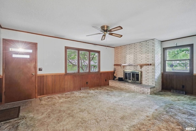 3816 Woodland Ct, Davenport, IA 52807 - unfurnished living room featuring wooden walls, crown molding, ceiling fan, a wainscoted wall, and a brick fireplace