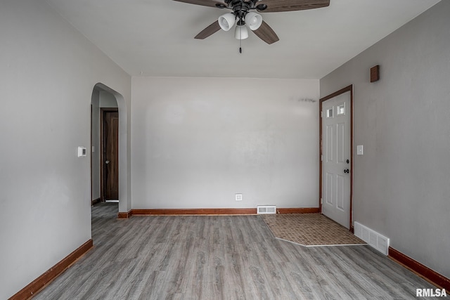 unfurnished room featuring wood finished floors, arched walkways, ceiling fan, and baseboards