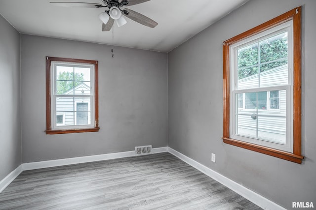 spare room featuring plenty of natural light, ceiling fan, wood finished floors, and baseboards