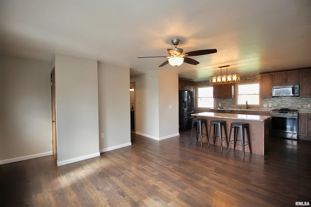 kitchen featuring appliances with stainless steel finishes, a center island, a kitchen bar, ceiling fan, and dark wood finished floors