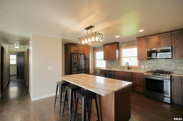 kitchen with appliances with stainless steel finishes, tasteful backsplash, a sink, dark wood-style floors, and a kitchen bar